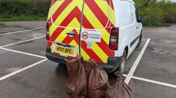 Three black bags filled with rubbish are piled up behind a South Hams District Council work van. The van is parked in a council car park bay.