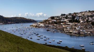 A photo of Salcombe Estuary and Town, as viewed from Snapes Point on a sunny day, with bright blue skies.