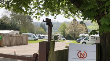 Campervans parked in Steamer Quay Caravan Park viewed from over the gate with the sign visible to the park.